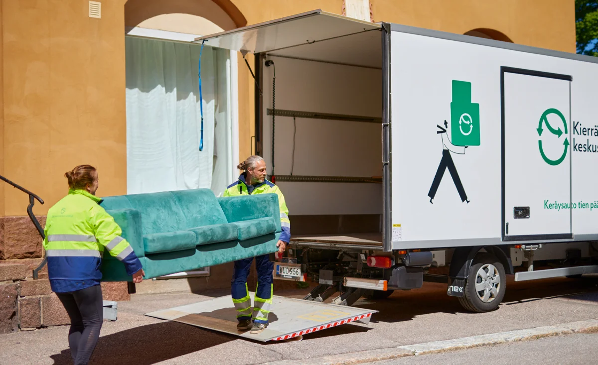 Kuljettavat kantavat sohvaa Kierrätyskeskuksen kuorma-autoon.